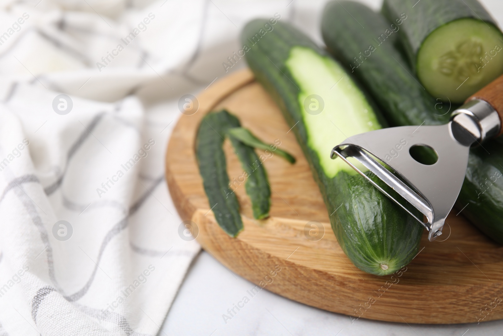 Photo of Fresh cucumbers and peeler on white table, closeup. Space for text