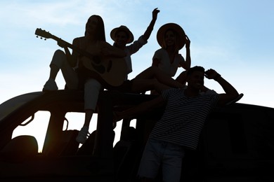 Image of Friends with guitar and car chilling outdoors. Silhouettes of people against blue sky