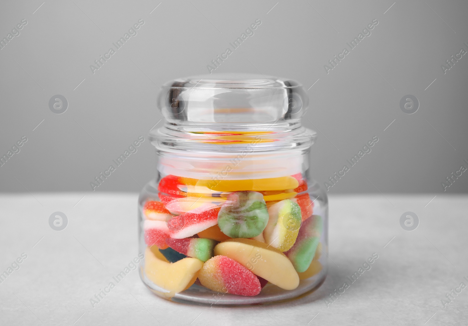 Photo of Tasty jelly candies in jar on light grey table, closeup