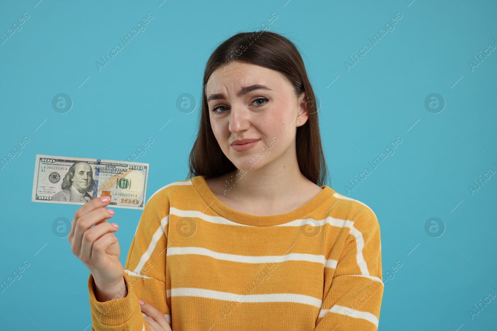 Photo of Sad woman with dollar banknote on light blue background