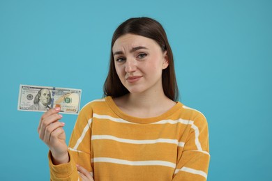 Photo of Sad woman with dollar banknote on light blue background