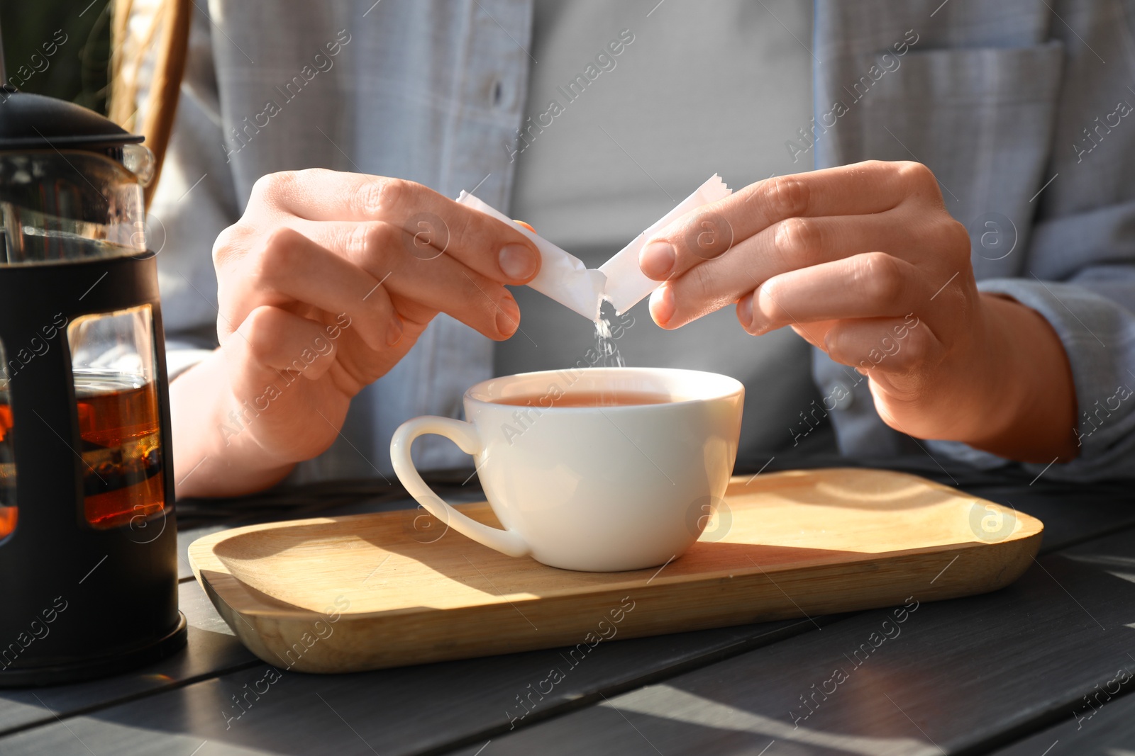 Photo of Woman adding sugar into cup of tea at black wooden table, closeup