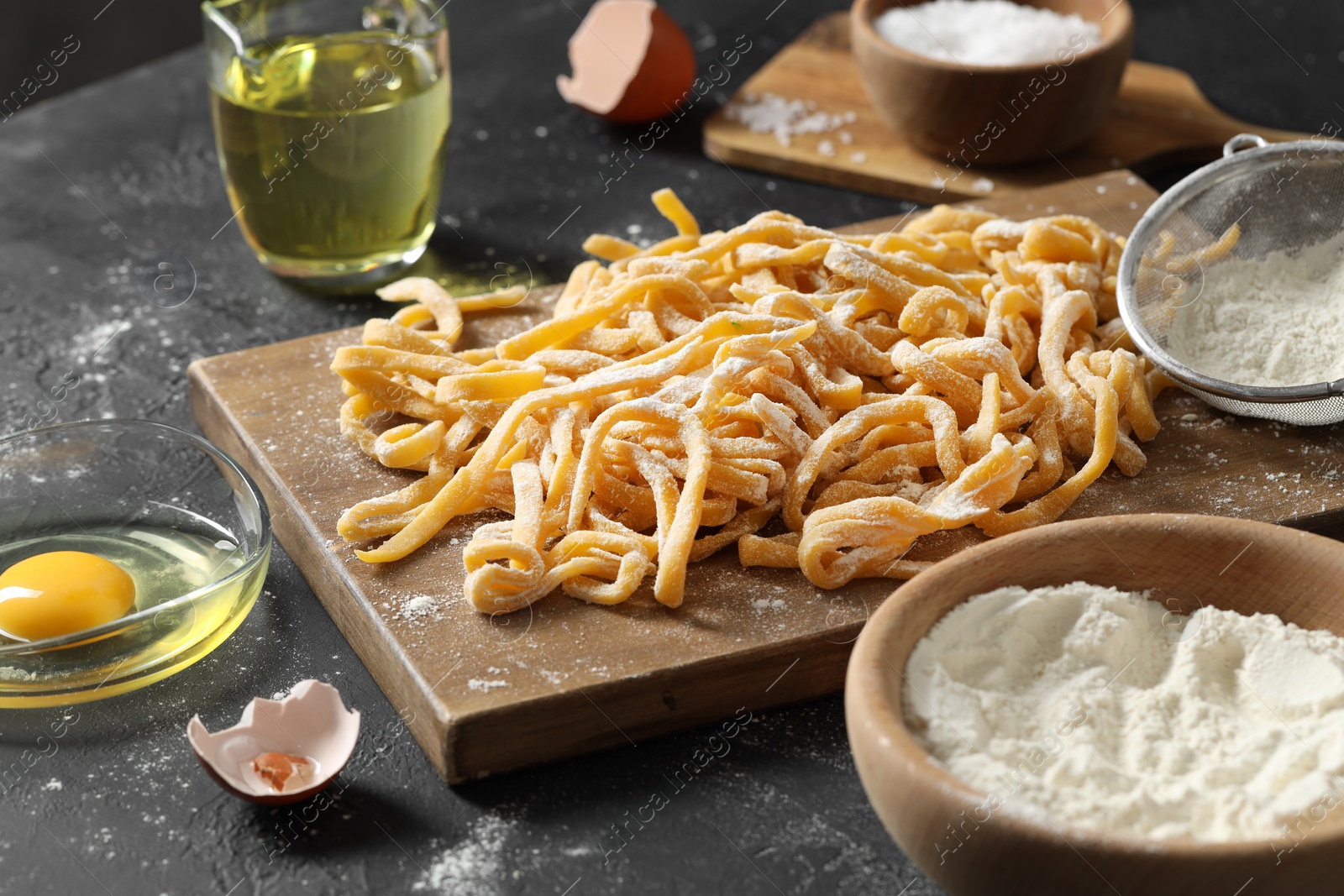 Photo of Board with homemade pasta, flour and ingredients on dark textured table