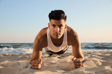 Photo of Sporty man doing plank on sandy beach