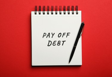 Image of Notebook with phrase Pay Off Debt and pen on red background, top view