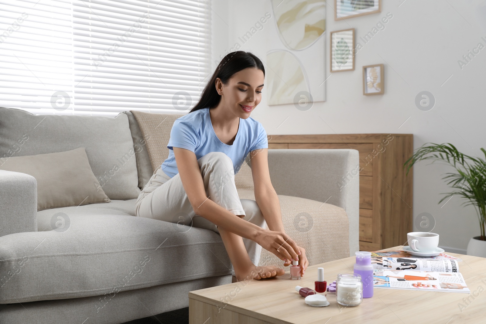 Photo of Beautiful young woman giving herself pedicure in living room