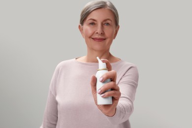 Woman holding nasal spray on light grey background, focus on bottle