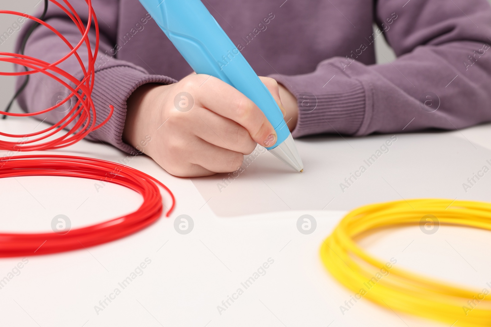 Photo of Boy drawing with stylish 3D pen at white table, closeup