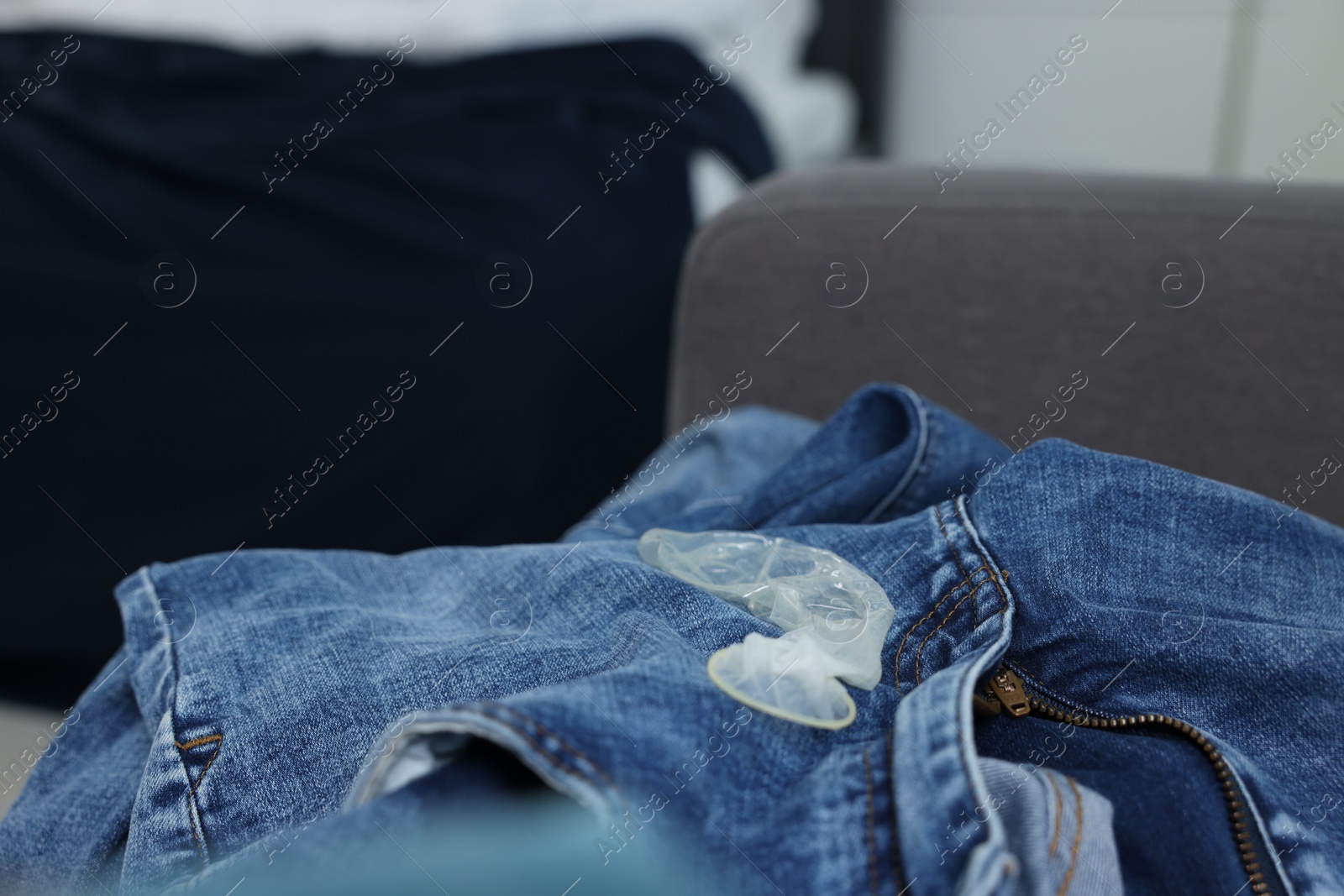 Photo of Unrolled condom and jeans in bedroom. Safe sex