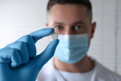 Doctor holding pill on light background, selective focus. Space for text