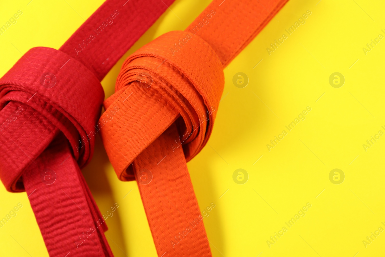 Photo of Red and orange karate belts on yellow background, flat lay. Space for text