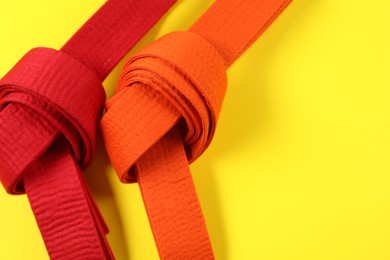 Photo of Red and orange karate belts on yellow background, flat lay. Space for text