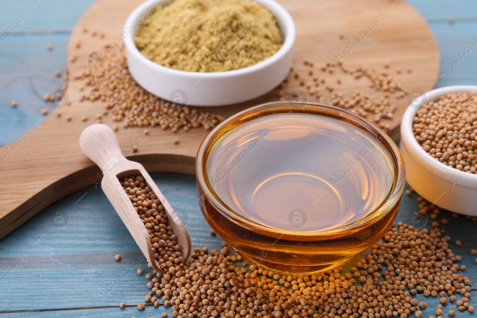 Bowl of natural oil, mustard seeds and powder on light blue wooden table, closeup Photo of Bowl of natural oil, mustard seeds and powder on light blue wooden table, closeup