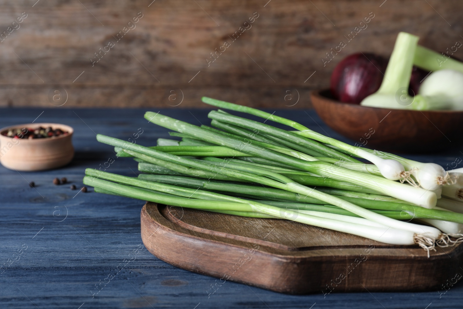 Photo of Wooden board with fresh green onion on blue table