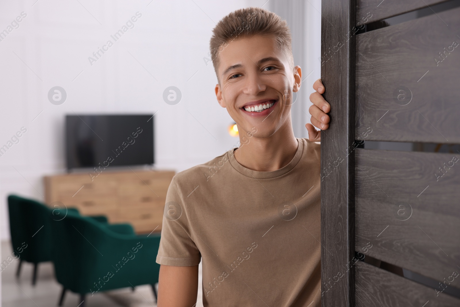 Photo of Happy man standing near door, space for text. Invitation to come indoors