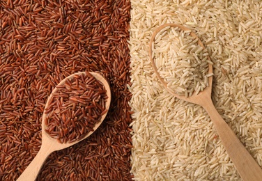 Photo of Wooden spoons with cereal on different types of brown rice, top view