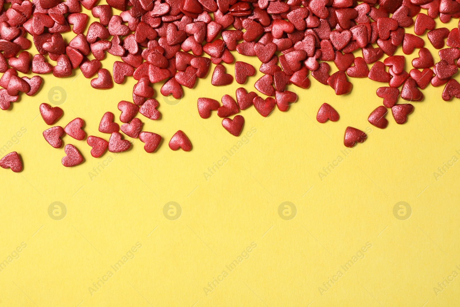 Photo of Bright heart shaped sprinkles on yellow background, flat lay. Space for text