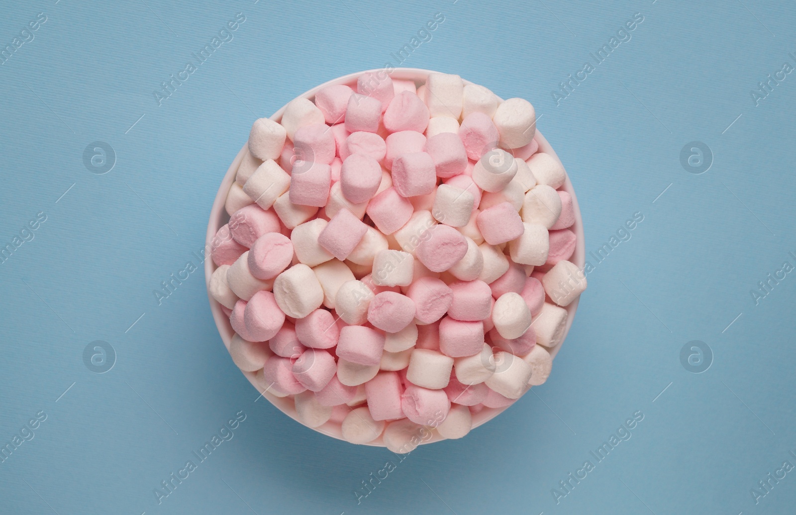 Photo of Bowl with delicious marshmallows on light blue background, top view