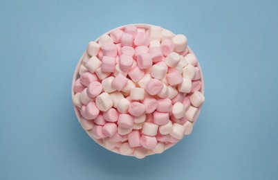 Bowl with delicious marshmallows on light blue background, top view