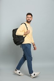 Young man with stylish backpack walking on light grey background