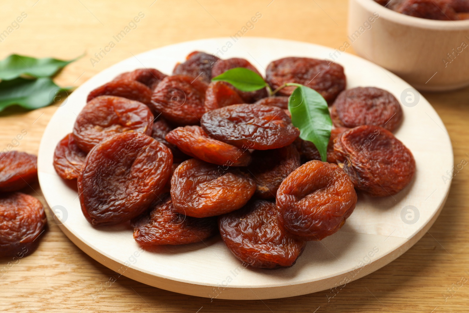 Photo of Plate of tasty apricots and green leaves on wooden table. Dried fruits