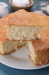 Photo of Plate with cut tasty sponge cake on light blue wooden table, closeup