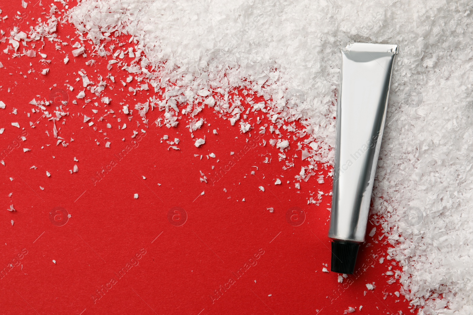 Photo of Winter skin care. Hand cream and artificial snow on red background, top view. Space for text