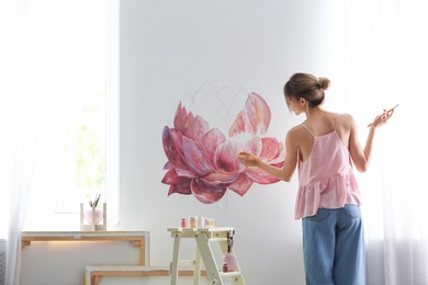 Photo of Decorator painting flower on white wall in room. Interior design