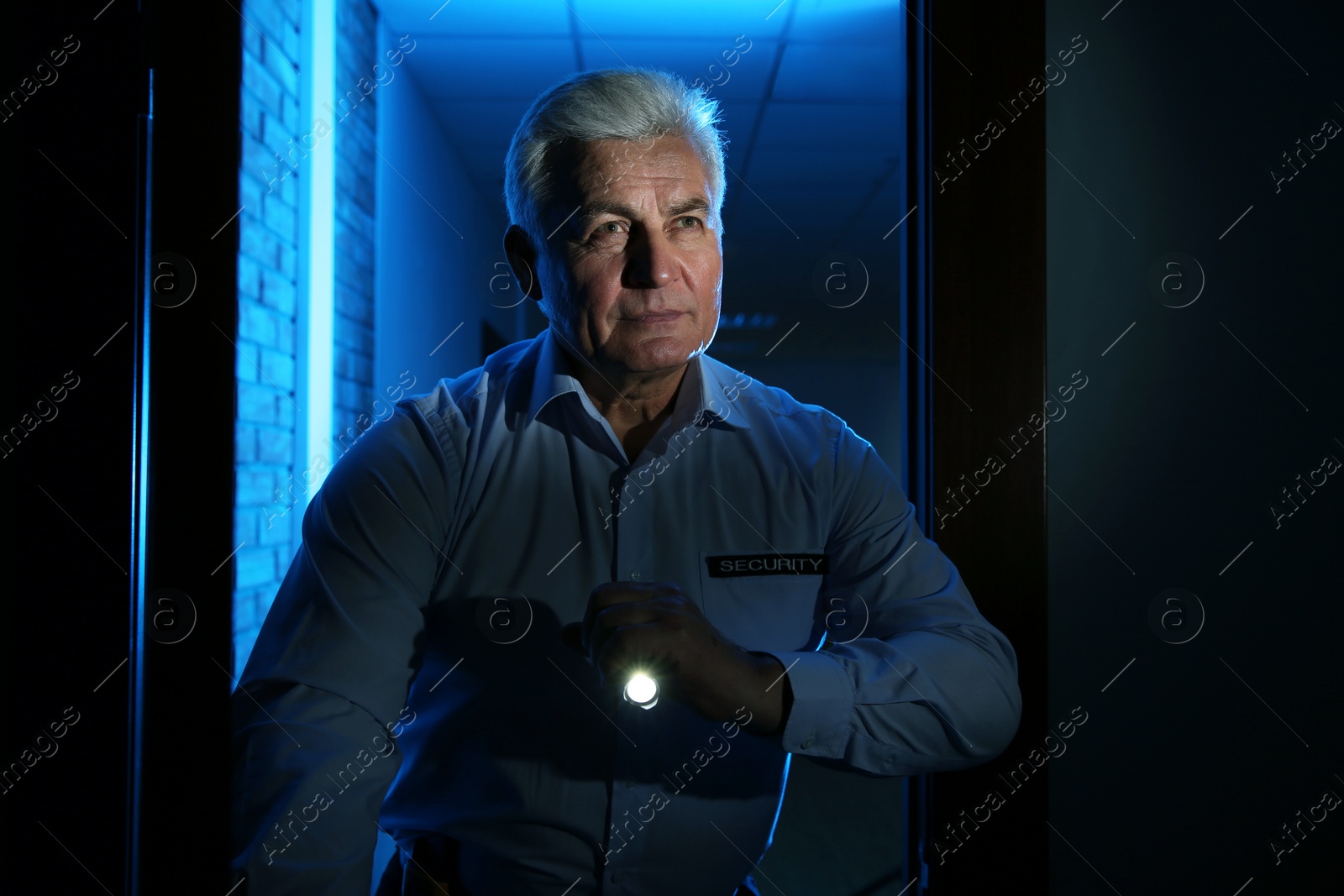 Photo of Professional security guard with flashlight checking dark room