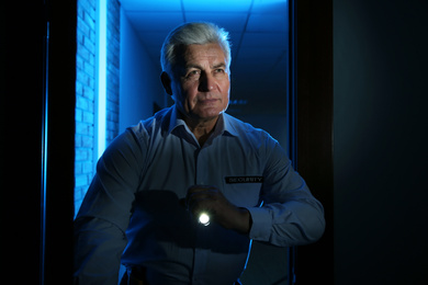 Photo of Professional security guard with flashlight checking dark room