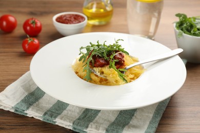 Photo of Tasty spaghetti squash with tomato sauce and arugula served on wooden table, closeup