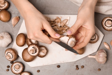 Photo of Young woman peeling fresh champignon mushrooms, top view