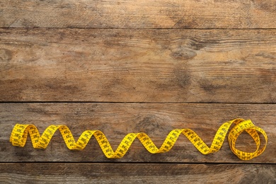 New yellow measuring tape on wooden table, top view. Space for text