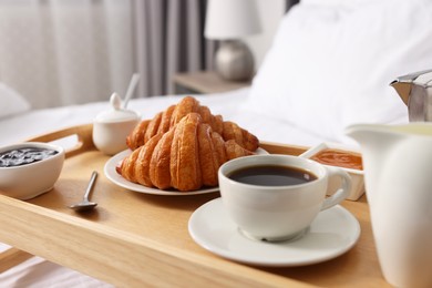 Photo of Wooden tray with tasty breakfast on bed at home, closeup