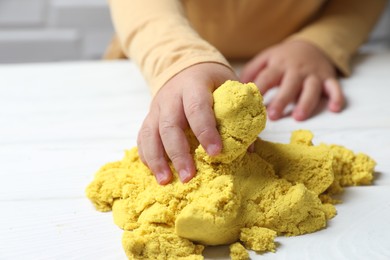 Little child playing with yellow kinetic sand at white wooden table, closeup