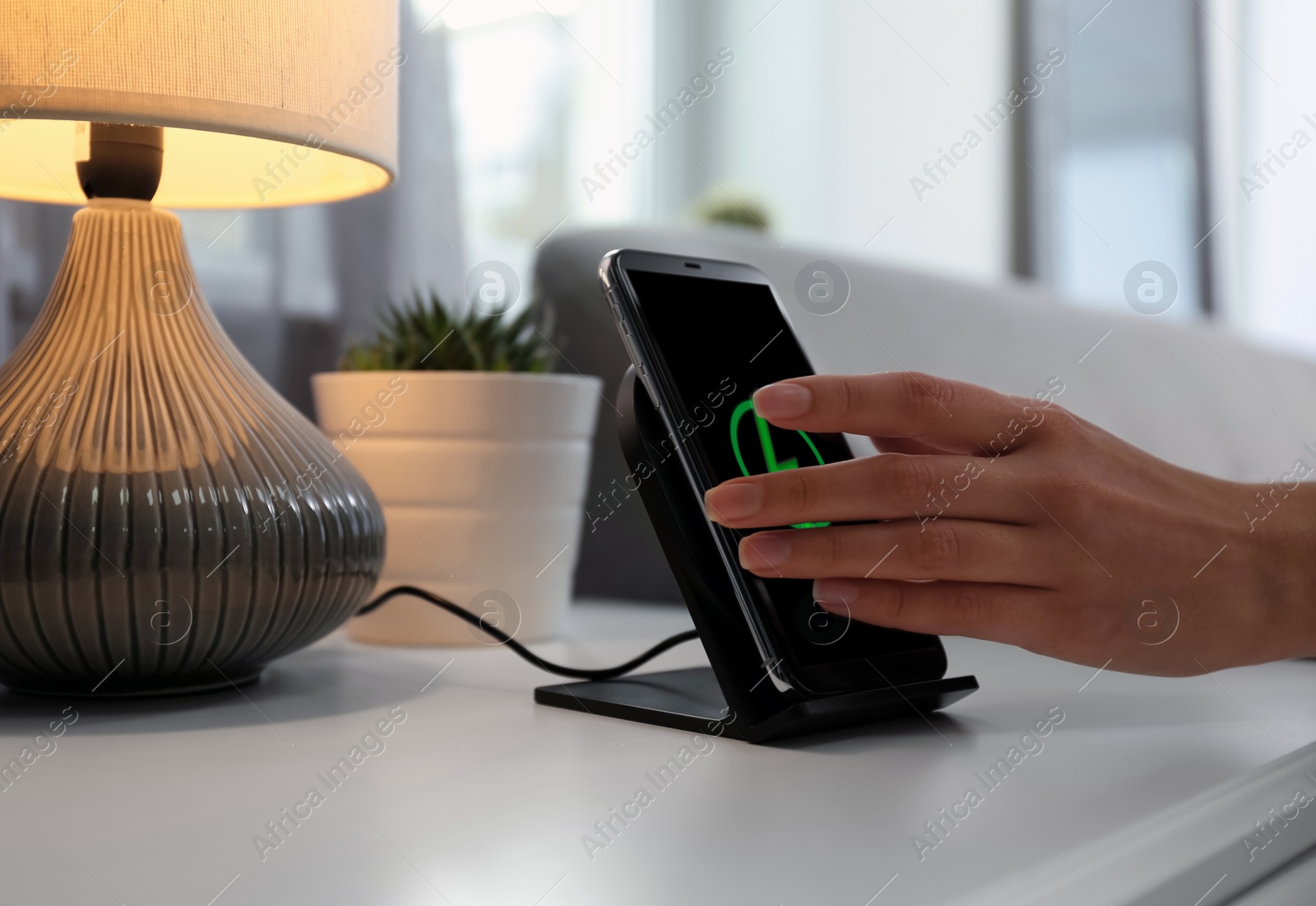 Photo of Woman taking smartphone from wireless charger in room, closeup