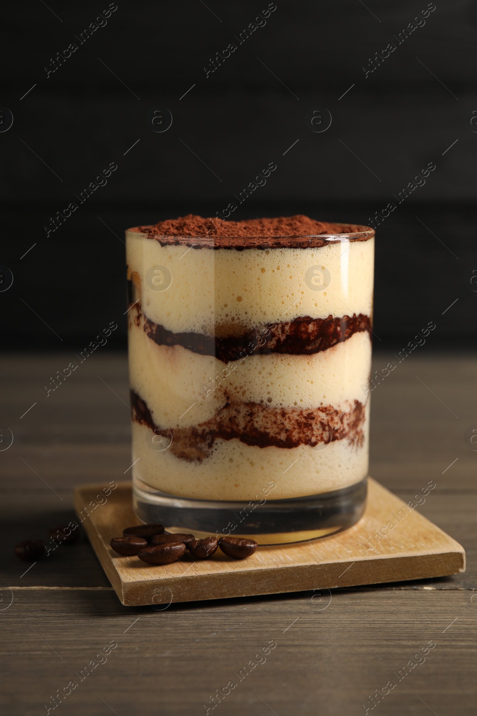 Photo of Delicious tiramisu in glass and coffee beans on wooden table