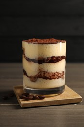 Photo of Delicious tiramisu in glass and coffee beans on wooden table