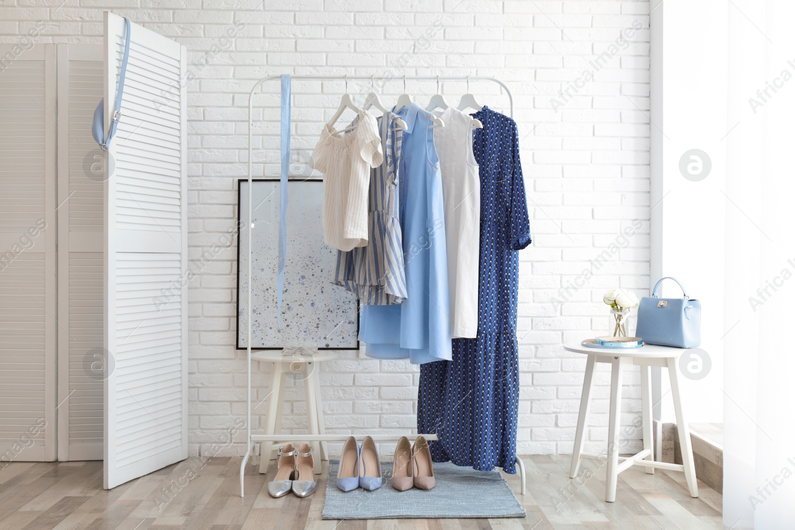 Photo of Wardrobe rack with women's clothes and different shoes at white brick wall in room