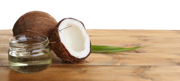 Ripe coconuts and jar with natural organic oil on wooden table against white background