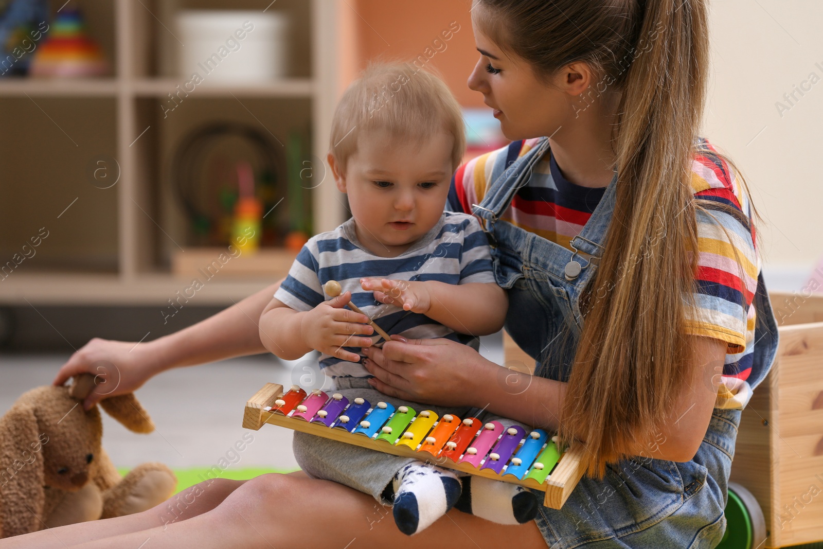 Photo of Teen nanny and cute little baby playing with xylophone at home