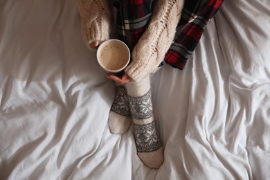 Woman with cup of coffee on soft blanket, top view