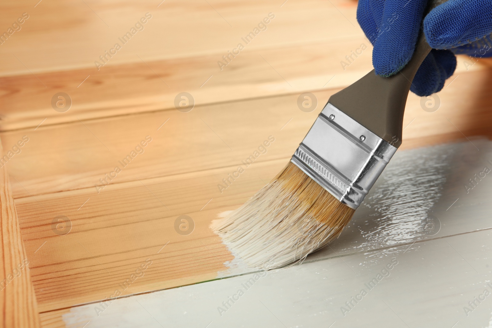 Photo of Worker applying white paint onto wooden surface, closeup. Space for text