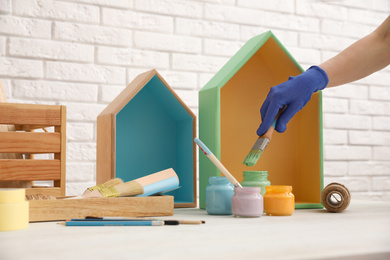 Photo of Decorator dipping brush into jar of green paint at white table, closeup