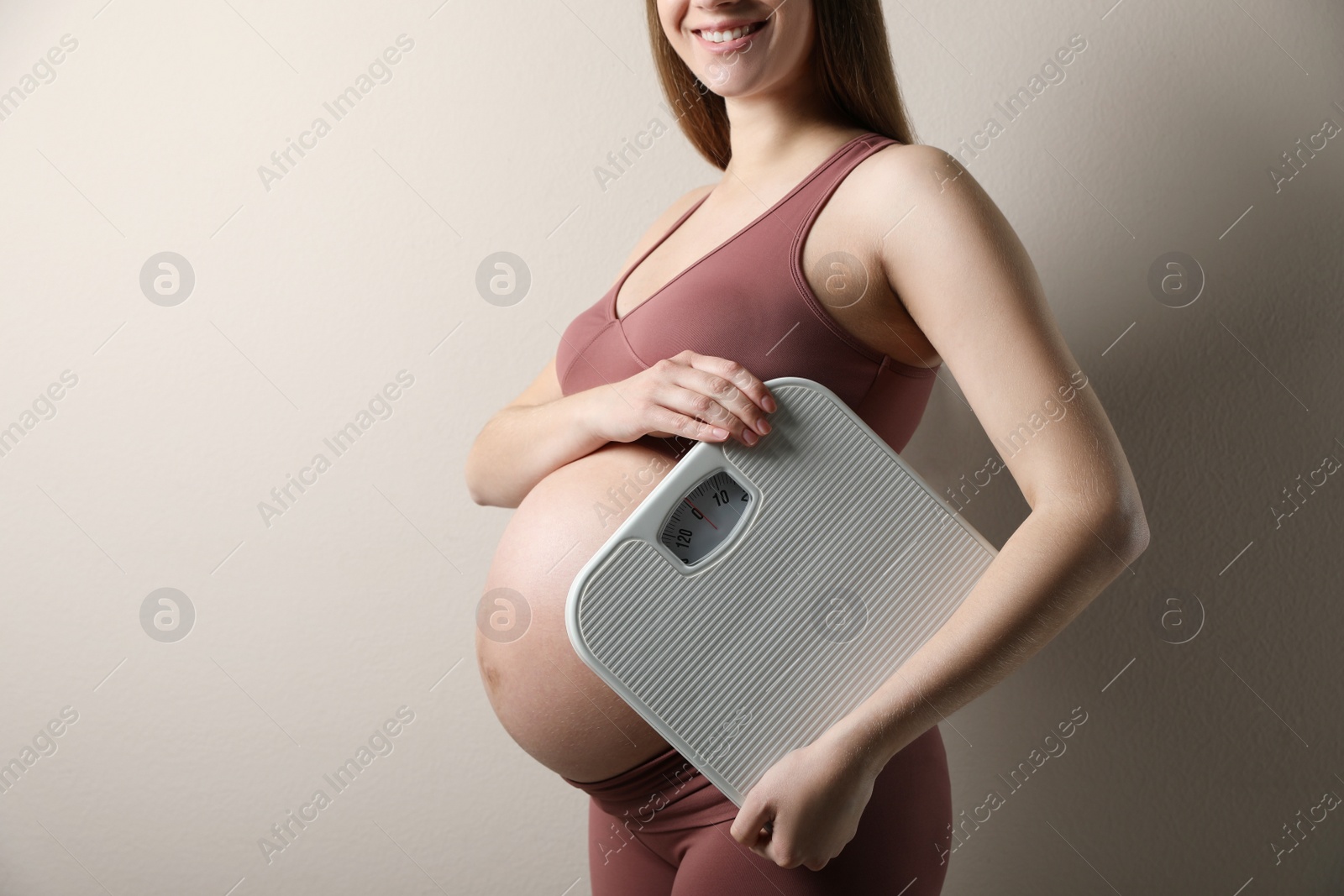 Photo of Pregnant woman with scales on beige background, closeup