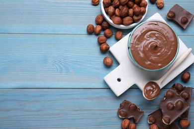Bowl with tasty paste, chocolate pieces and nuts on light blue wooden table, flat lay. Space for text