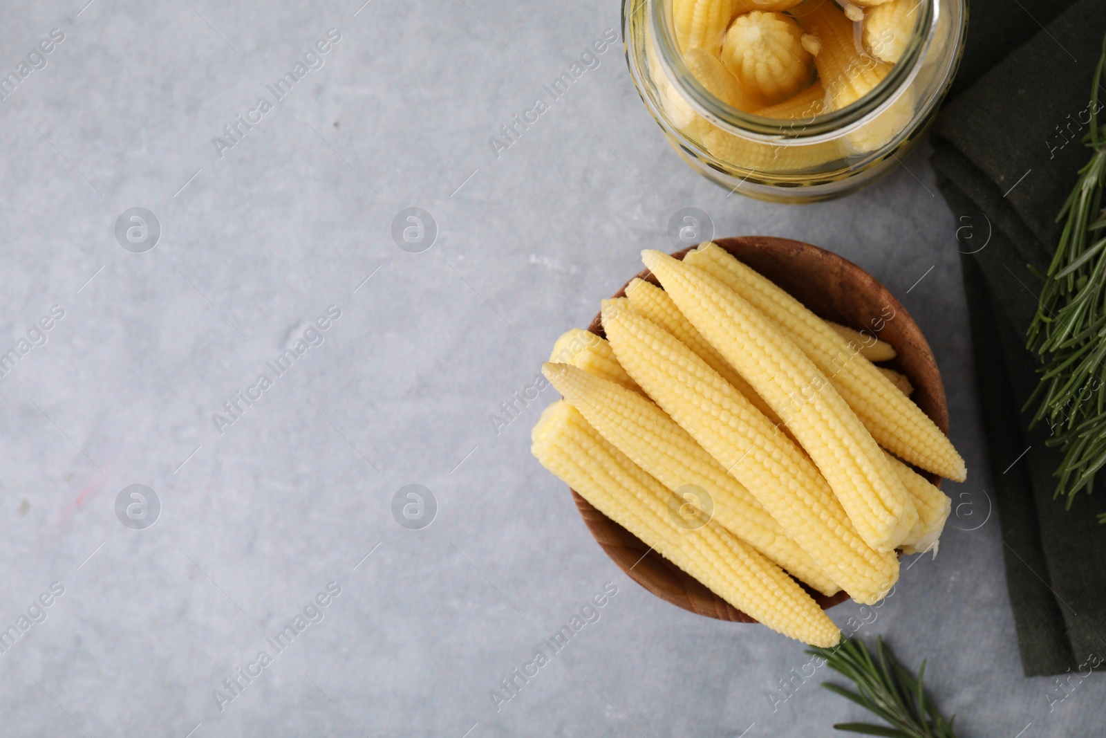 Photo of Tasty fresh yellow baby corns in bowl on grey table, top view. Space for text