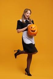 Photo of Happy woman in scary maid costume with carved pumpkin on orange background. Halloween celebration