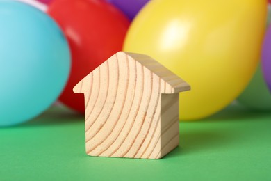 Photo of Wooden house model and balloons on green background. Housewarming party