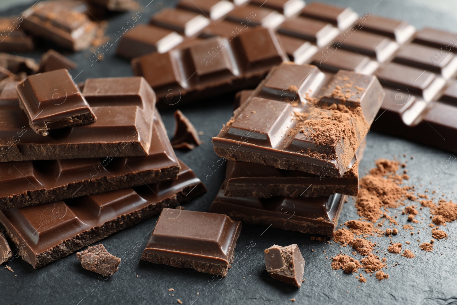 Photo of Pieces of tasty chocolate on slate plate, closeup